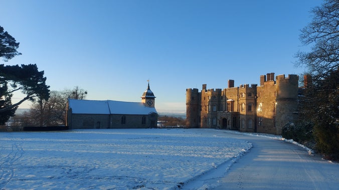 The driveway leading up to Croft Castle, with the road, lawn, and castle covered in snow.